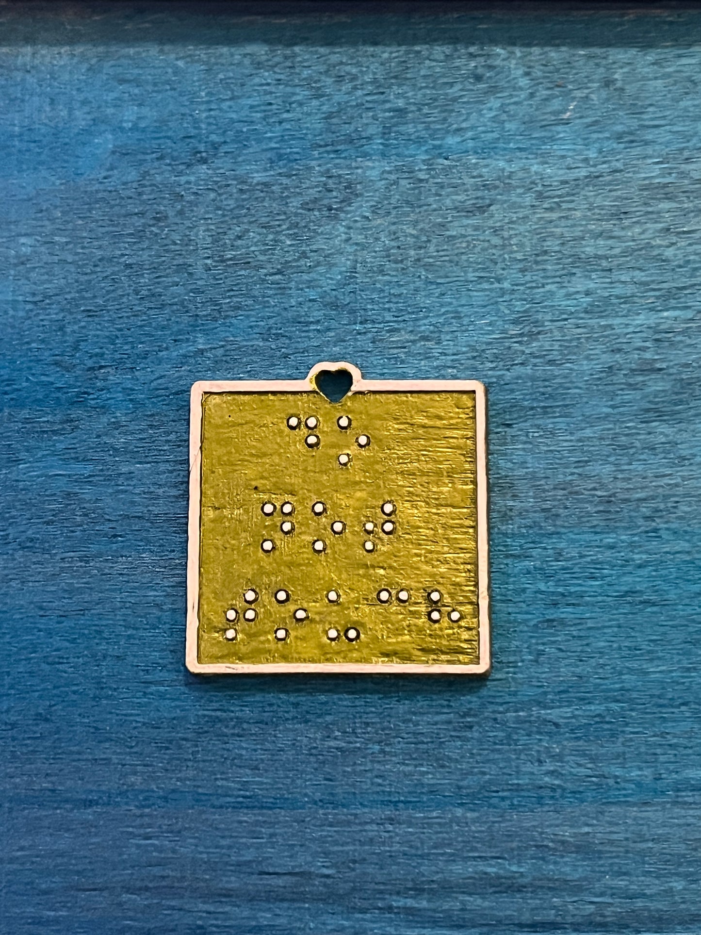 One inch square metallic olive green wooden pendant with “do not touch” in  white braille.